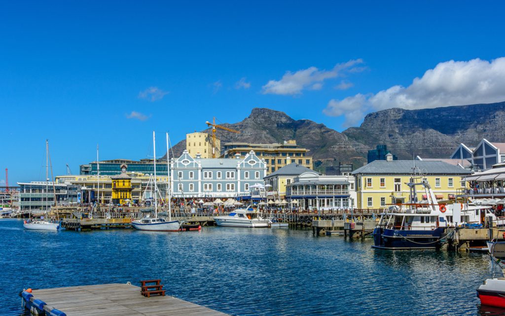 Panoramic view of Table Mountain, Cape Town, South Africa, seen from V&A Waterfront with clock tower, boats in the harbor, blue sky and clouds.