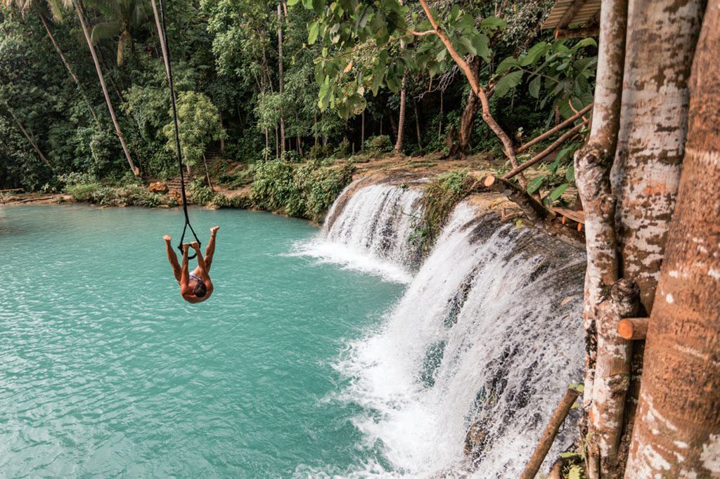Young man playing on a rope swing over Cambugahay Falls, Siquijor Island, Philippines