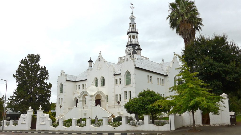 A white and red church surrounded by trees in Swellendam, South Africa.