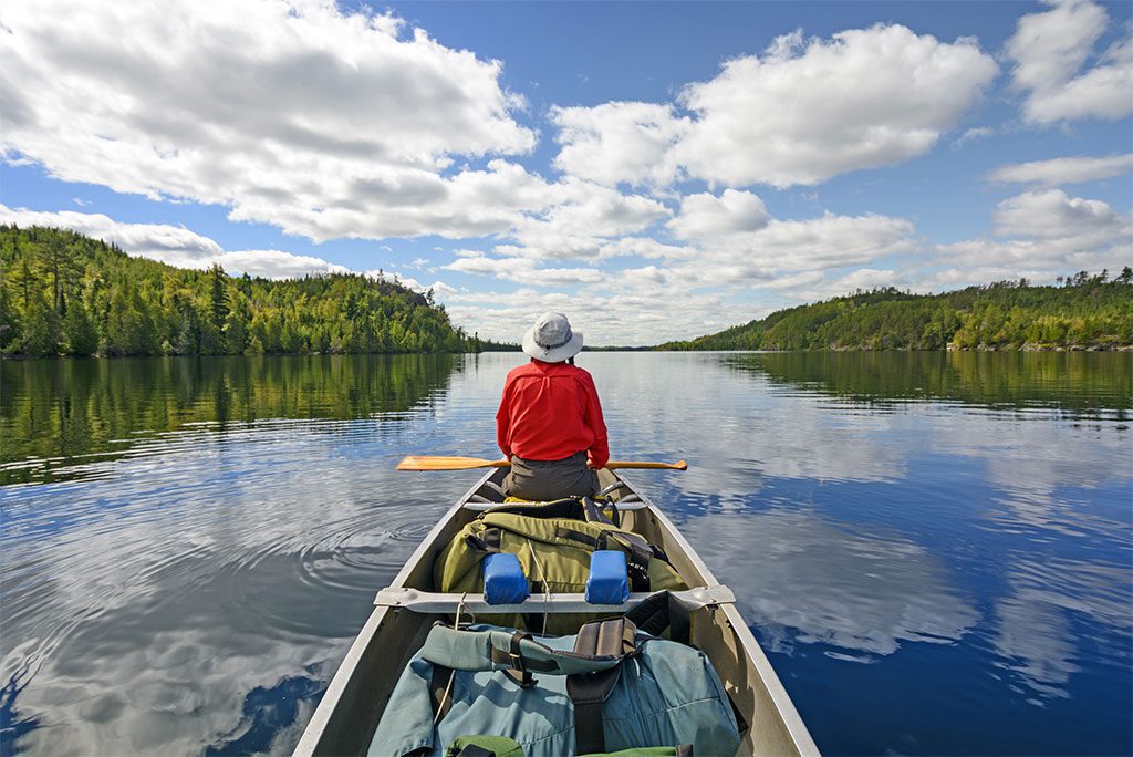 : A person canoeing on a lake surrounded by trees and mountains.