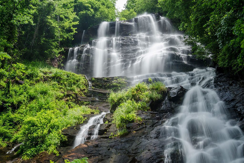 Waterfall cascading over rocks and surrounded by trees and foliage.