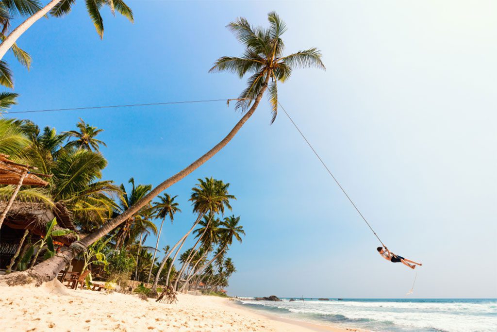 A boy having fun swinging on a rope at a tropical island beach in Sri Lanka