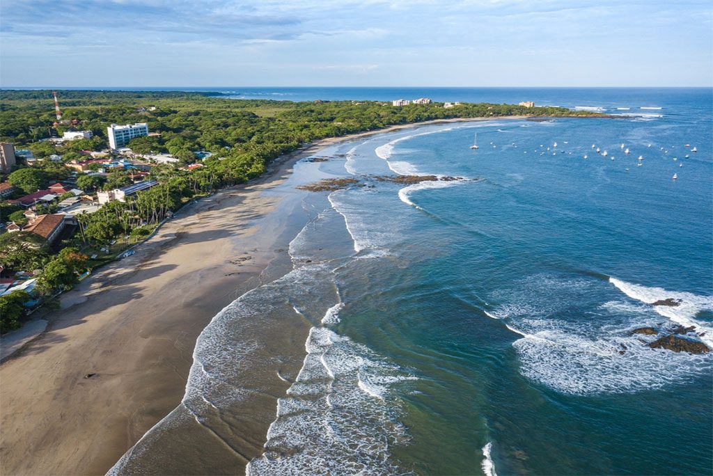 Aerial view of Tamarindo Beach in Guanacaste, Costa Rica with turquoise waters and palm trees.