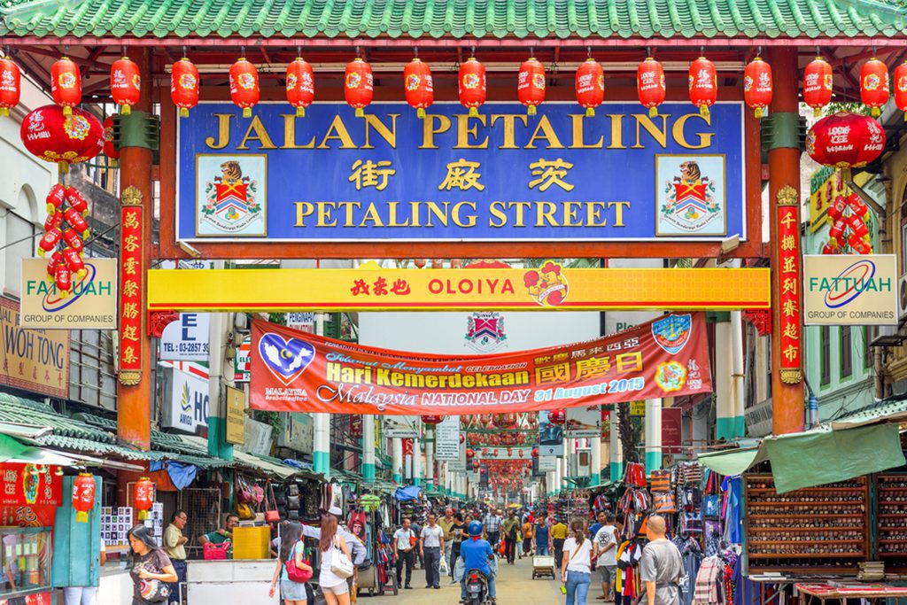 Crowds pass below the main gate of Chinatown at Petaling Street