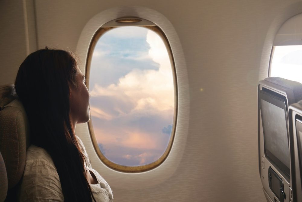 A woman relaxing on a comfortable plane seat, gazing out the window at the clouds, symbolizing travel, vacation, and transport.