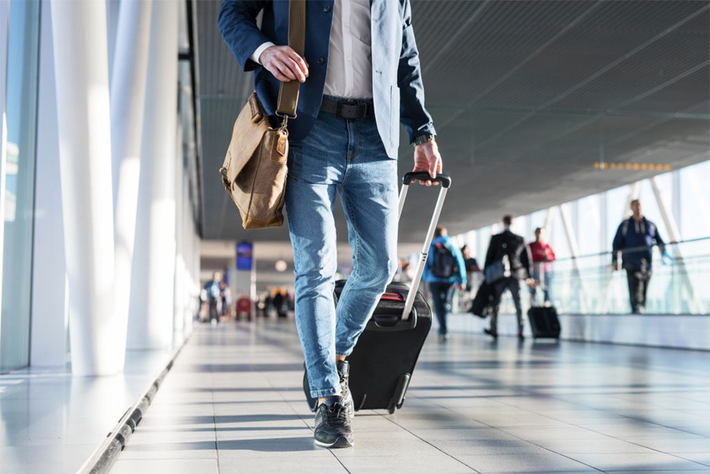 A man with a shoulder bag and hand luggage walking in an airport terminal.