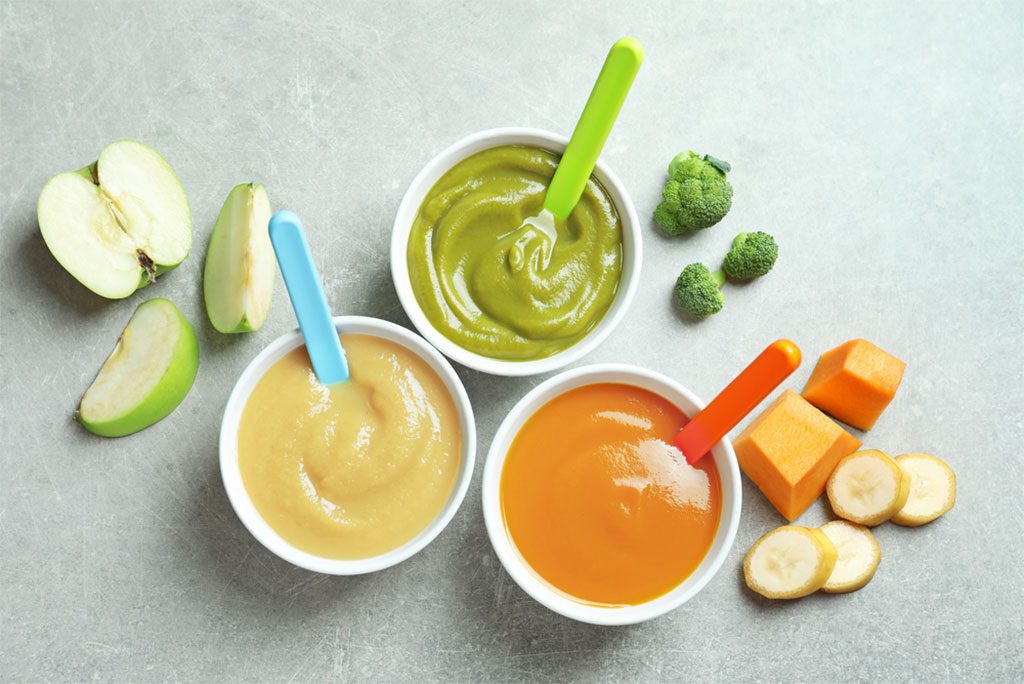 Bowls filled with colorful and nutritious baby food on a grey background