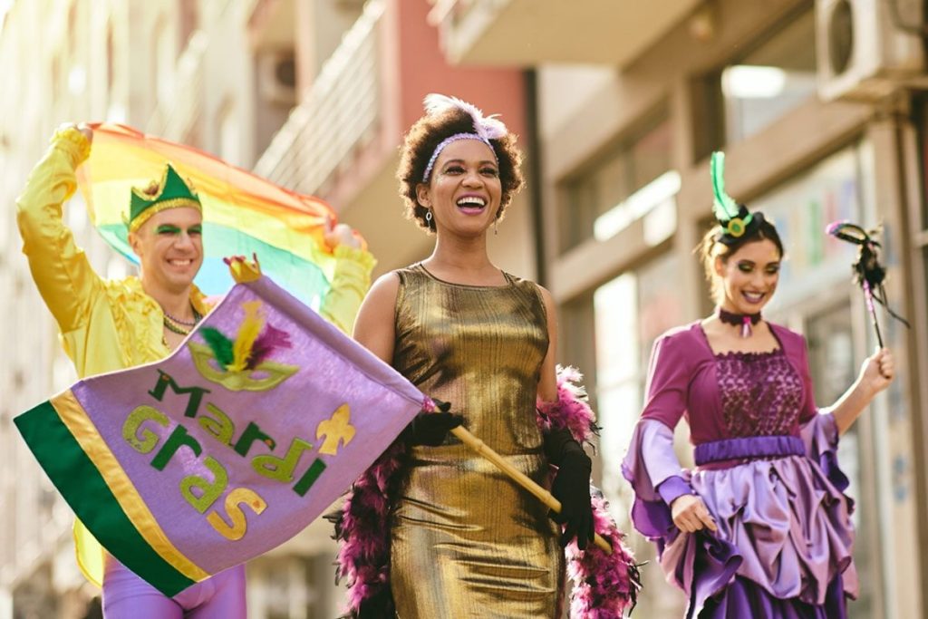 Happy African American woman and her friends wearing colorful carnival costumes and makeup during the Mardi Gras parade