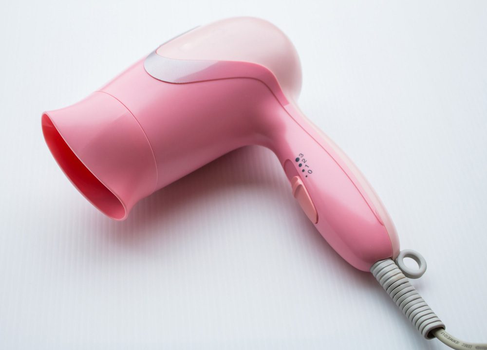 An image of a small pink hairdryer isolated on a white background