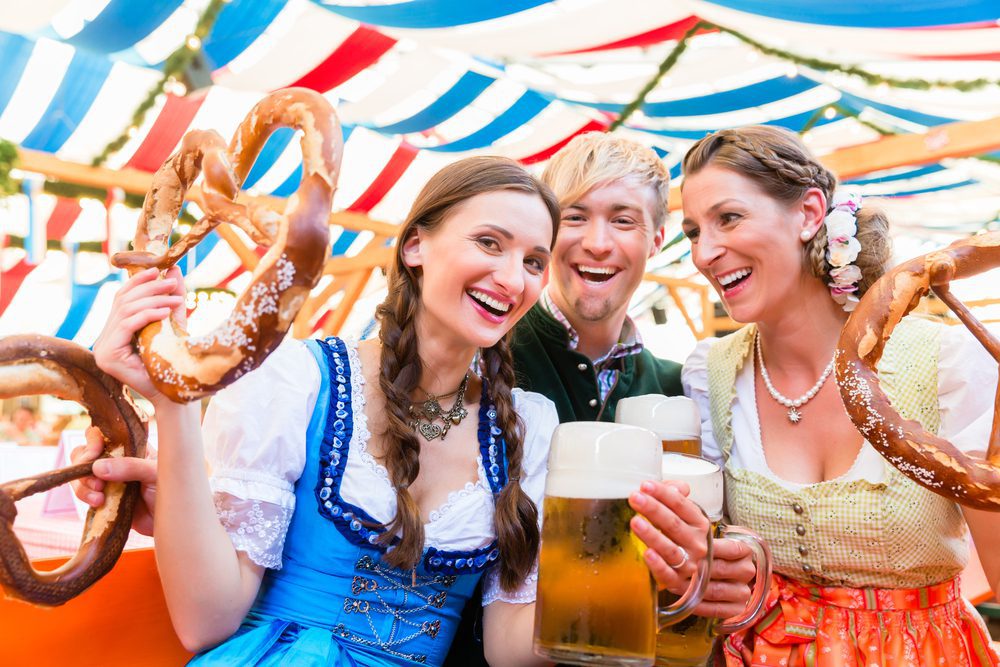 Three friends raising giant pretzels in a beer tent during Dult or Oktoberfest.