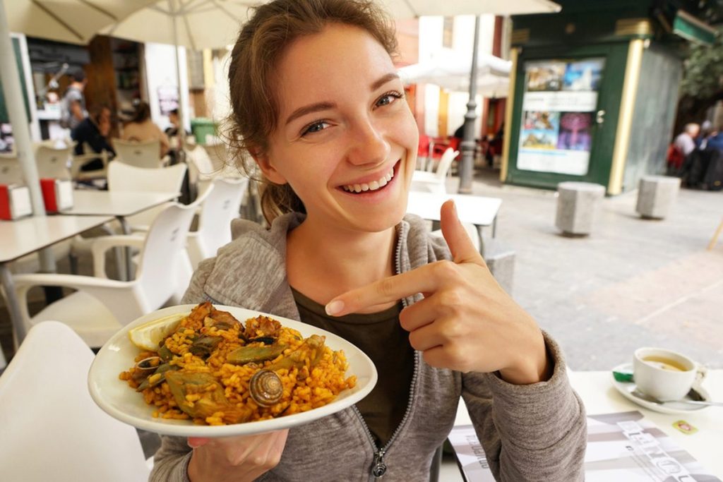 Smiling woman pointing to a plate of delicious paella at an outdoor restaurant in Spain
