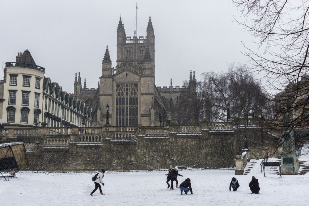 Children playing in the snow in front of Bath Abbey, England - a delightful winter activity.